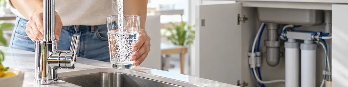 acqua microfiltrata cos’è Bicchiere riempito dal rubinetto con sistema di microfiltrazione visibile sotto il lavello.