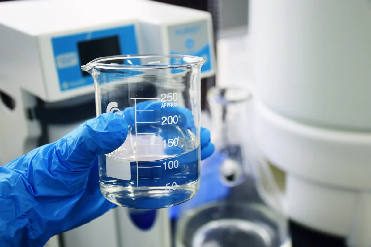 Mano con guanto che tiene un becher con un campione d'acqua da analizzare in laboratorio